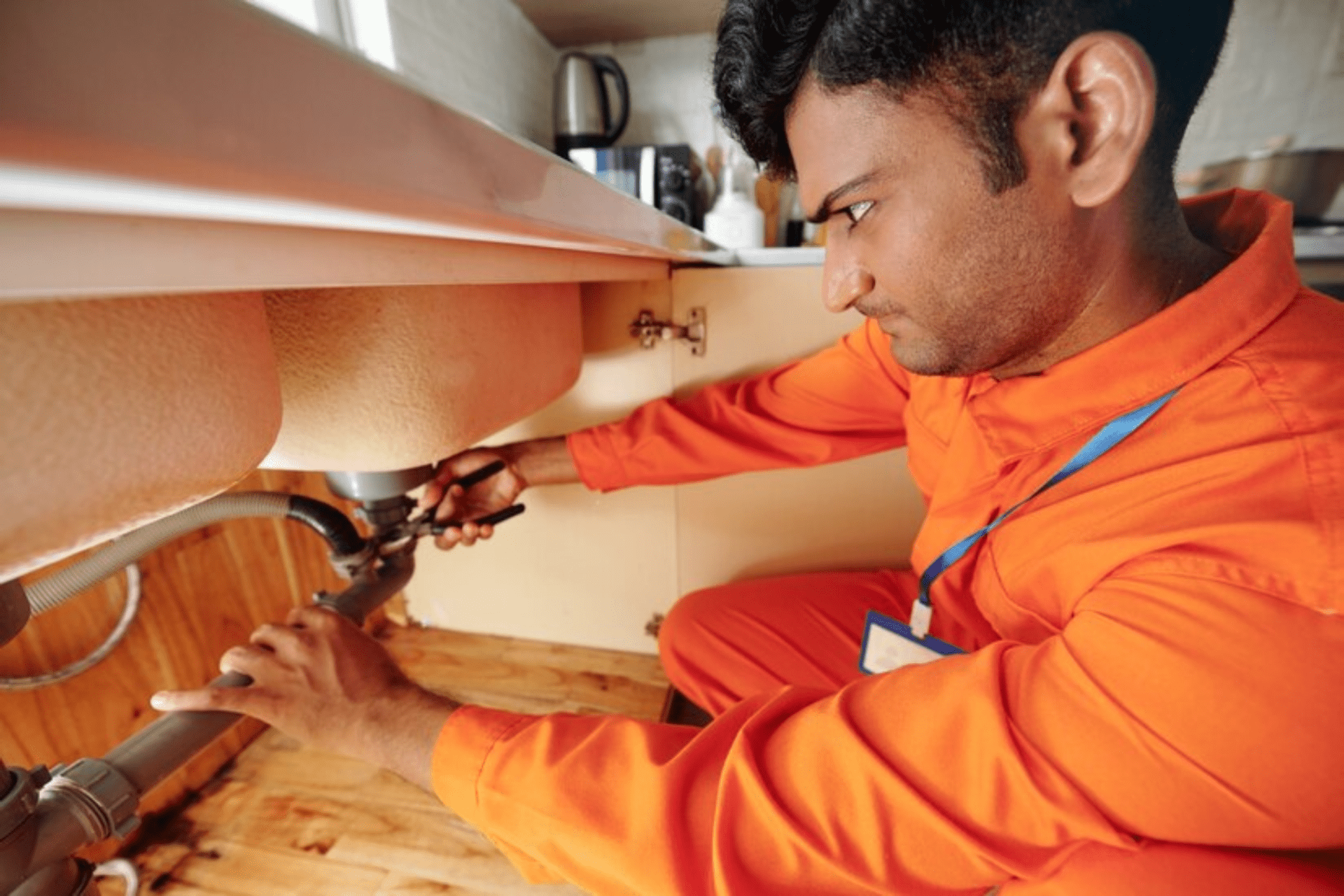 Serious handyman using pliers when fixing leaking pipe under sink in kitchen of customer